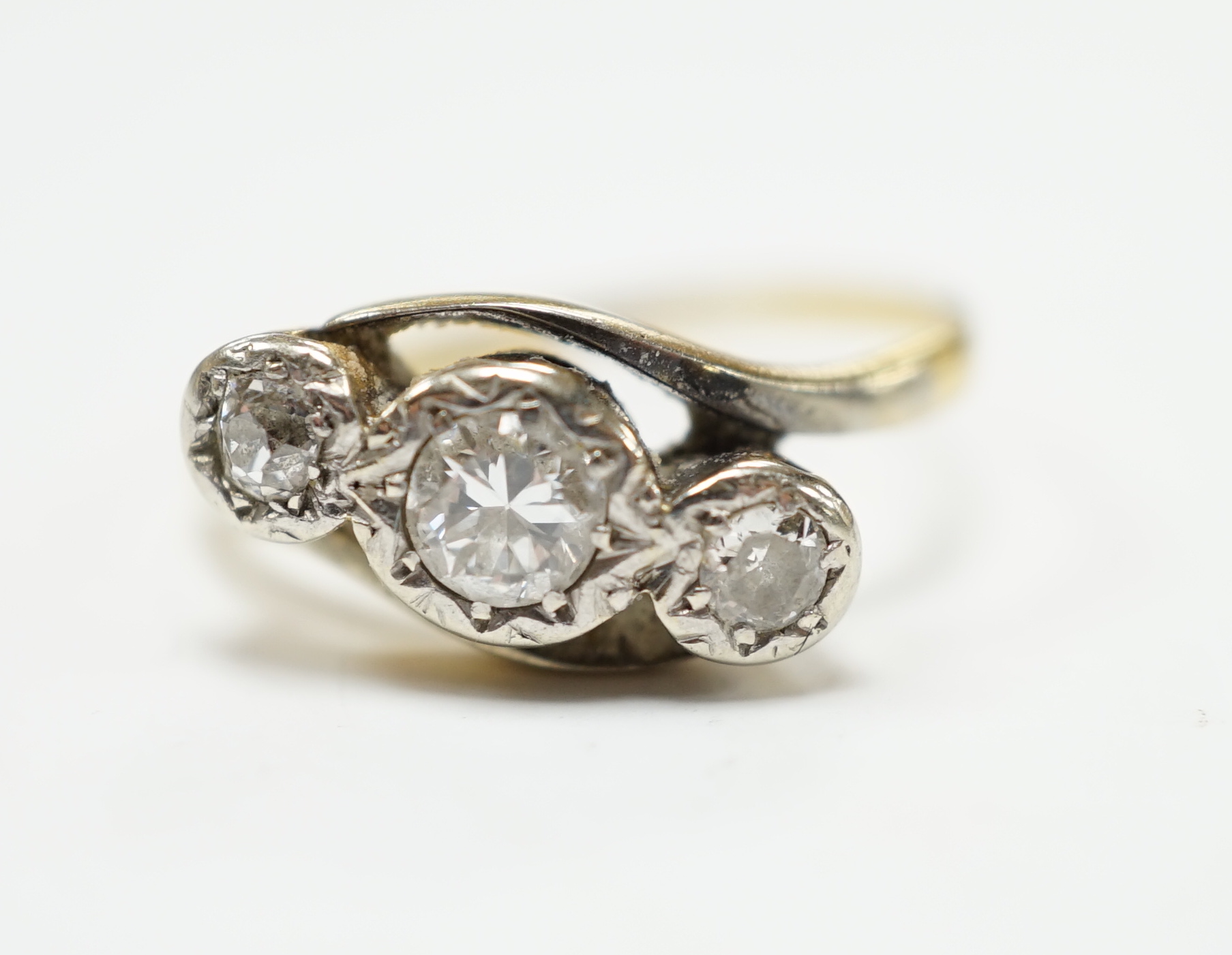 A yellow metal and illusion set three stone diamond set crossover ring, size O/P, gross weight 3.2 grams.